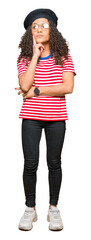 Obraz premium Young beautiful woman with curly hair wearing glasses and fashion beret with hand on chin thinking about question, pensive expression. Smiling with thoughtful face. Doubt concept.