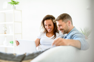 Fototapeta premium bearded husband cuddling affectionate wife on computer at home. Using laptop in living room.