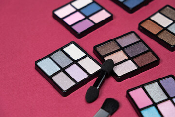 A set of multi-colored eyeshadow and brushes on a pink background. Eye makeup