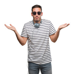 Handsome young man wearing headphones clueless and confused expression with arms and hands raised....