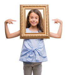 Fototapeta premium Brunette hispanic girl holding vintage art frame very happy pointing with hand and finger