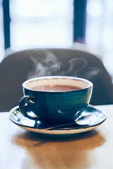 A cup of freshly brewed black tea, rising steam, warm soft light, against the background of a window in a cafe. High quality photo
