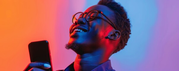 Fototapeta premium Joyful man with glasses holding a smartphone against vibrant neon lights, enjoying a moment of happiness and connection.