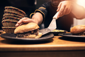 Chef, person and hands in kitchen with burger, fast food and preparation on table. Male cook, meal and dinner of sandwich, order and culinary for hospitality service with cooking for professional