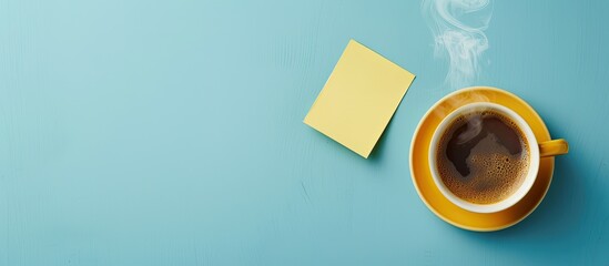 A steaming cup of coffee beside a Good Morning sticky note on blue backdrop with ample copy space for top-down view capturing.