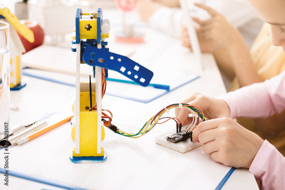 Poster a young girl is shown concentrating as she carefully connects wires to a robotic arm. she is working