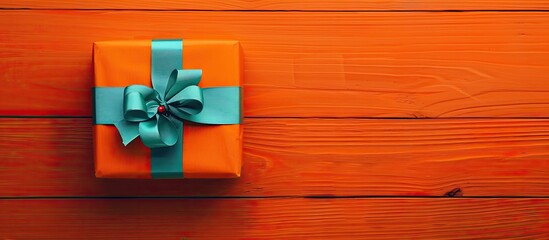 A lovely present box with a colorful ribbon on an orange wooden surface, seen from above with a blank area for your design, embodying a Christmas theme.