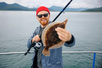 Happy Scandinavian fisherman caught flounder fish with fishing rod, trip north ocean