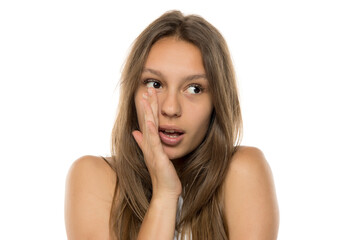 Fototapeta premium Young woman is holding hand near mouth and telling a secret on a white background