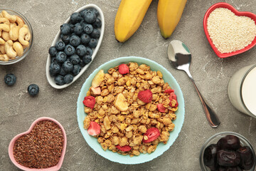 Granola with strawberries in a bowl with berries on grey background.