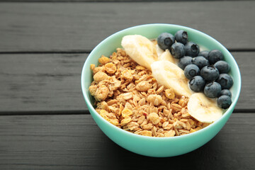 Oat raisin granola with fresh summer berries in a bowl on black wooden background. Concept of healthy breakfast food, clean eating, dieting