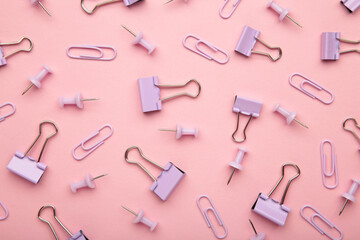 Set of purple paper clips, binders and pins on pink background