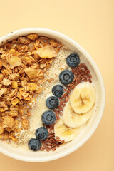 Oat raisin granola with fresh summer berries in a bowl on beige background. Vertical photo