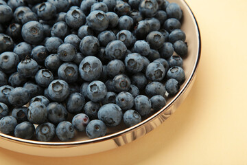 Beige ceramic bowl of fresh ripe blueberries on beige background. Macro photo