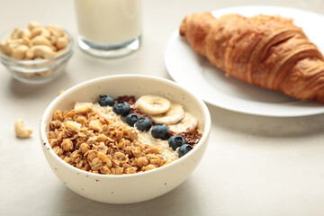 Beautiful morning breakfast with fresh croissants, granola with yoghurt and berries and fruit on plate. Tasty and healthy breakfast on white wooden table