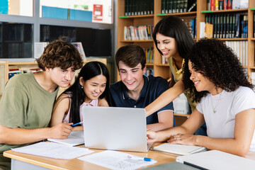 Diverse group of five high school students studying together using laptop at library. Millennial college friends working together on university task.