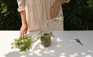 A woman pours oil into a jar with St. John's wort flowers. Close up.