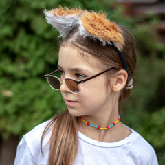 Close-up of a little cute girl in sunglasses and fur ears looking into the distance
