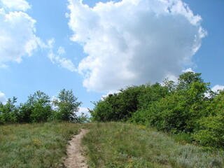 Obraz premium A panorama of a trodden path going up the hillside against the background of amazing cloud patterns on the sky horizon.