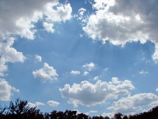 Obraz premium A natural picture of the sun's rays in the blue sky coming out of the illuminated cloud in straight lines and illuminating the surrounding clouds of various shapes.