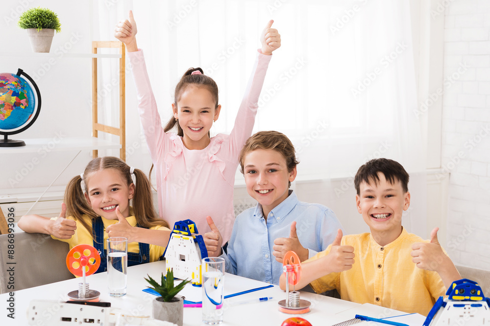 Poster four young students, two girls and two boys, sit at a table in a classroom setting with thumbs up af