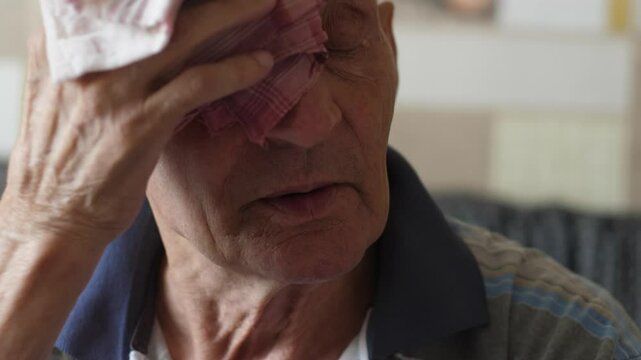 Caucasian elderly man 70 -79 years old wipes sweat from his forehead with a handkerchief while inside