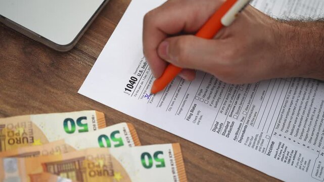 Small business owner fills out Income Tax Return form reporting business income and expenses to calculate tax owing using at table with few euro bills