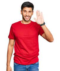 Fototapeta premium Young handsome man wearing casual red tshirt waiving saying hello happy and smiling, friendly welcome gesture