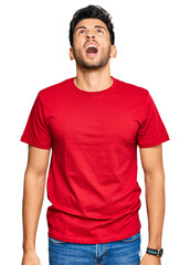 Young handsome man wearing casual red tshirt angry and mad screaming frustrated and furious, shouting with anger. rage and aggressive concept.