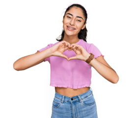 Hispanic teenager girl with dental braces wearing casual clothes smiling in love doing heart symbol shape with hands. romantic concept.