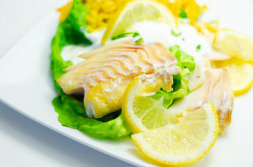 A plate of food with a fish fillet, rice, and lemon slices