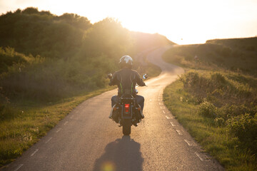 Biker driving a motorcycle rides along the asphalt road in sunset. © erika8213