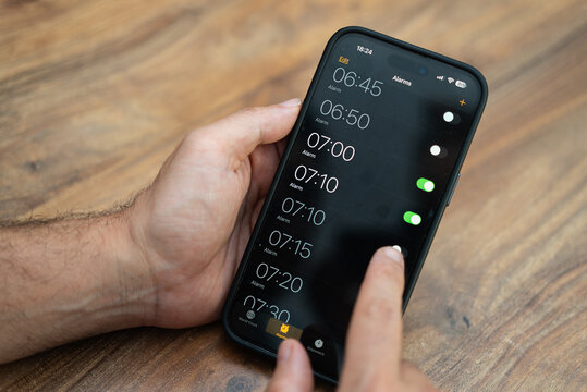 Male person holds modern smartphone setting time on alarm clock app ensuring to receive timely notifications to wake up early in morning for productive working day