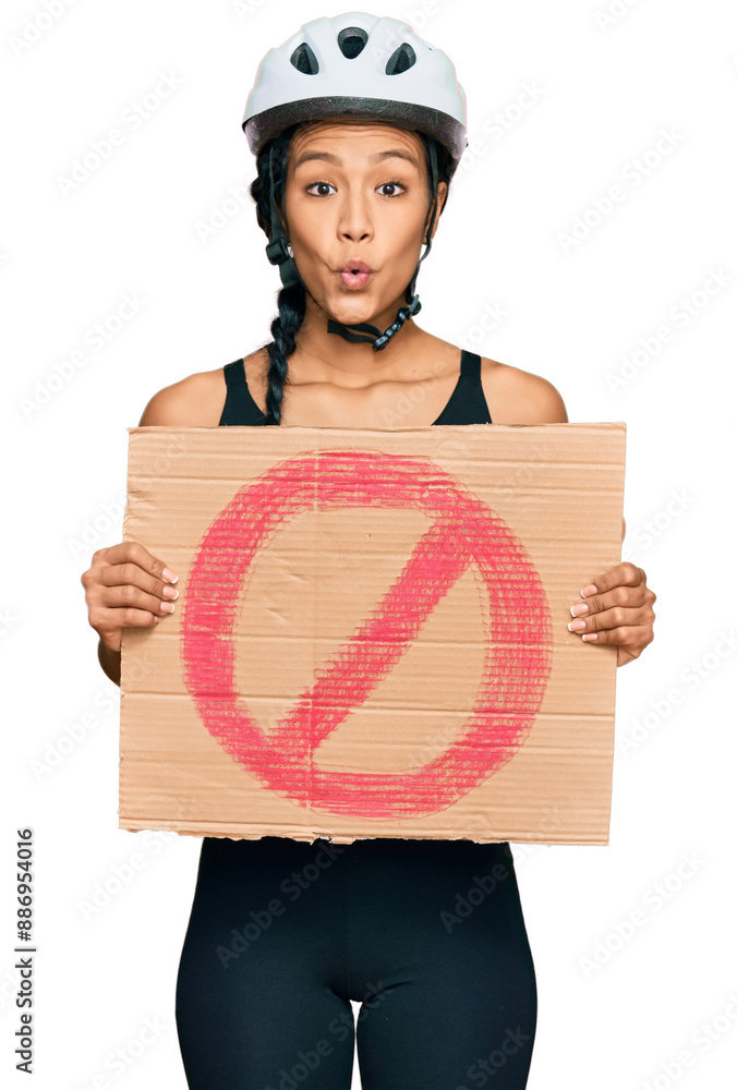 Sticker beautiful hispanic woman wearing bike helmet and holding stop banner scared and amazed with open mou