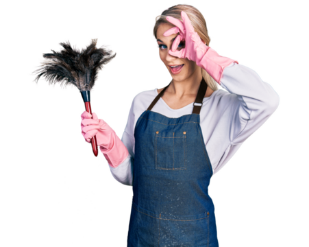 Beautiful young blonde woman wearing apron holding cleaning duster doing ok gesture with hand smiling, eye looking through fingers with happy face.