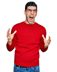 Handsome hispanic man wearing casual clothes and glasses crazy and mad shouting and yelling with aggressive expression and arms raised. frustration concept.