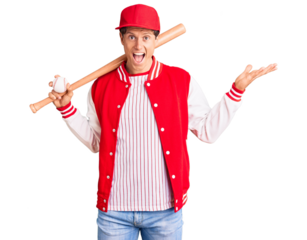 Young handsome man playing baseball holding bat and ball celebrating victory with happy smile and winner expression with raised hands