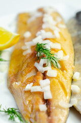 A smoked fish fillet with onions and lemon slices on top
