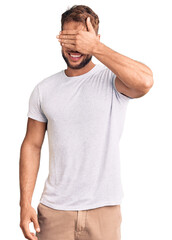 Young caucasian man wearing casual white tshirt smiling and laughing with hand on face covering eyes for surprise. blind concept.