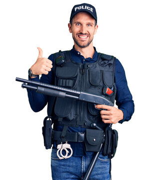 Young handsome man wearing police uniform holding shotgun smiling happy and positive, thumb up doing excellent and approval sign