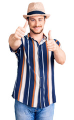 Young handsome caucasian man wearing summer hat approving doing positive gesture with hand, thumbs up smiling and happy for success. winner gesture.