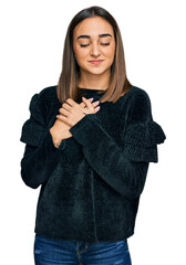Beautiful brunette woman wearing elegant sweater smiling with hands on chest with closed eyes and...