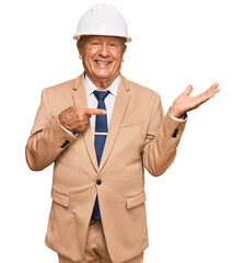 Senior caucasian man wearing architect hardhat amazed and smiling to the camera while presenting with hand and pointing with finger.
