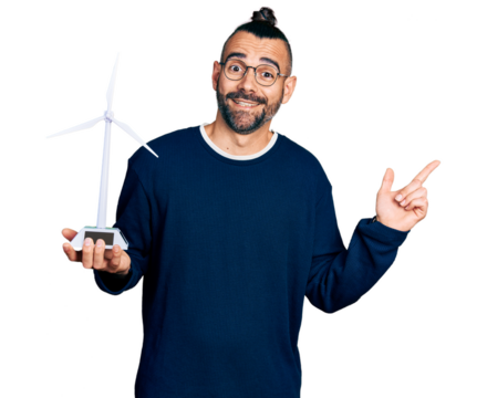 Hispanic man with ponytail holding solar windmill for renewable electricity smiling happy pointing with hand and finger to the side