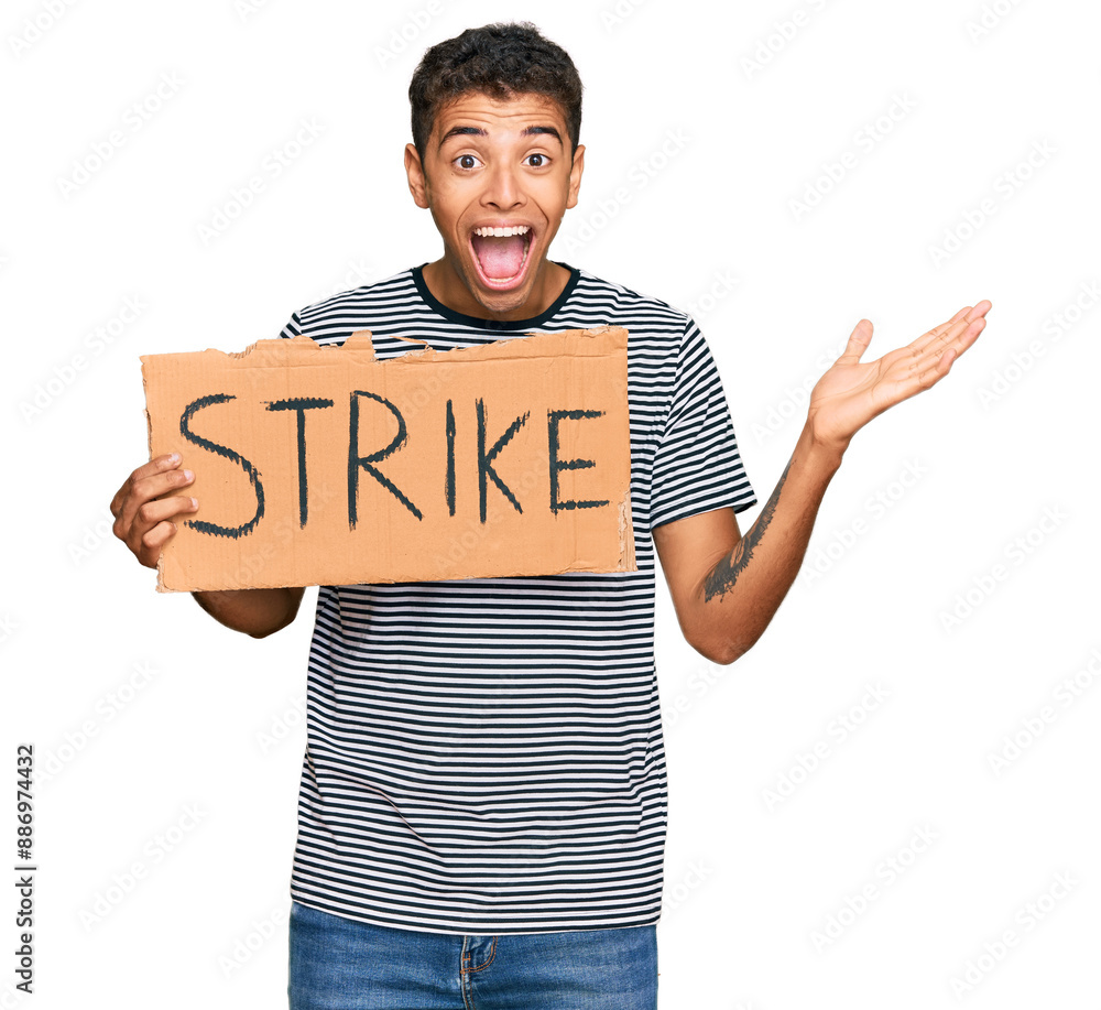 Sticker Young handsome african american man holding strike banner cardboard celebrating victory with happy smile and winner expression with raised hands