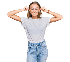 Beautiful young blonde woman wearing casual white t shirt smiling pulling ears with fingers, funny gesture. audition problem