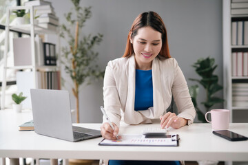 Businesswoman analyzing investment charts with laptop and using calculator at office. Female entrepreneur is smiling and examining financial report