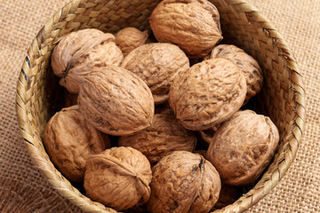 Organic unshelled walnuts as a source of protein and fiber in a rustic wicker bowl on rough burlap. Whole nutritious nuts. Top view