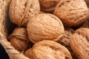 Mature whole walnuts with textured hard shells in a rustic wicker bowl. Macro shot. Healthy organic nuts