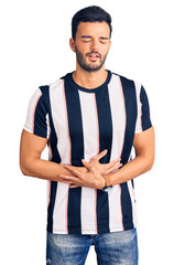 Young handsome hispanic man wearing striped tshirt with hand on stomach because nausea, painful disease feeling unwell. ache concept.